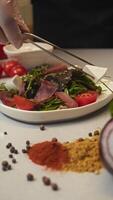 Chef arranges pieces of cheese over bed of vegetables and slices of meat, creating a light and low-calorie gourmet dish. Vertical video