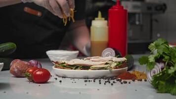 Chef of restaurant in gloves sprinkles grated cheddar cheese on crispy toast with various vegetables and chicken meat cut into thin slices. process of making sandwich video