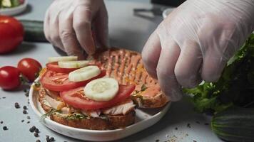 Cook prepares sandwich by covering filling of vegetables and chicken with other half of the bread, in order to complete the sandwich and make it ready for serving to customers in restaurant. video