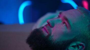 Close up side view of a bearded man looking up and thinking of something. Media. Young man with neon light on the background. video