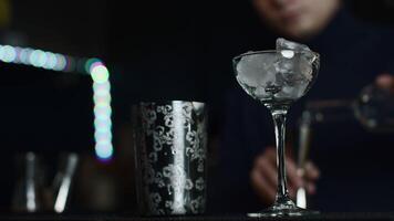Close up of glass with ice cubes prepared for cocktail. Media. Bartender mixing alcohol liquids in a shaker. video