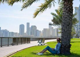 Happy tourist relaxing on lawn under palm tree in Sharjah while looking at camera. Vacation and sightseeing concept photo