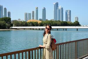 The skyline of Sharjah is visible from the waterfront - a woman tourist with a backpack enjoys the view of the water and skyscrapers. Cityscape of Sharjah UAE. photo