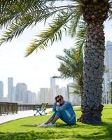 Happy tourist relaxing on lawn under palm tree in Sharjah while looking at camera. Vacation and sightseeing concept photo