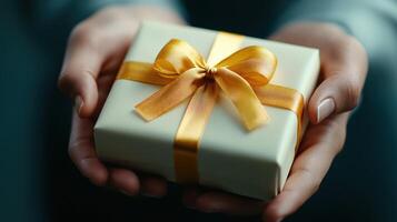 person holds cream gift box with golden ribbon, expressing joy photo