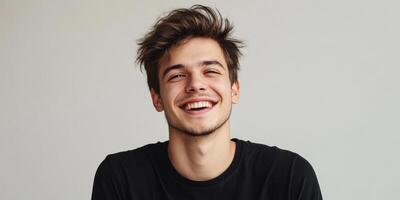Portrait of a joyful young man with bright eyes and a radiant smile, dressed in a black t-shirt and having a trendy hairstyle, set against a light gray background. Copy space is available. photo