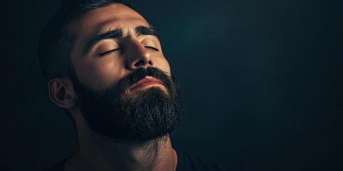 un barbado hombre con su ojos cerrar y un sereno expresión es conjunto en contra un oscuro estudio fondo con Copiar espacio. foto