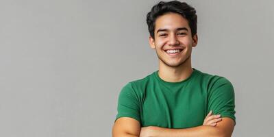 Portrait of a Hispanic Latino man with crossed arms and black hair, smiling as a handsome young adult in a green t-shirt against a gray background, looking at the camera in a studio shot. photo