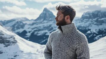 man in cozy sweater stands in snowy mountain landscape, gazing thoughtfully at majestic peaks under cloudy sky photo