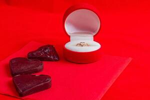 A chocolate heart on a red napkin with a ring in a box on a red background photo