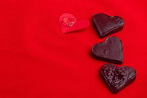 A diamond ring on a red paper heart with chocolate hearts on a red background photo