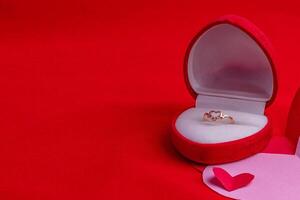ring box with diamonds on a hand-cut paper heart on a red background photo