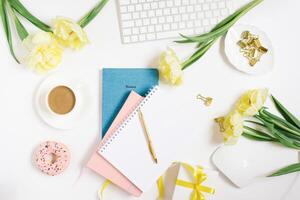 Office workspace with a white desk. Top view from above with a keyboard, notepad, gift, flowers and pencil with a white cup of coffee on a plate. Flat surface with copy space. Women's business concept photo