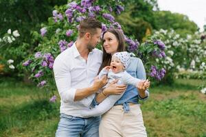 Portrait of a Caucasian family enjoying happy love, father and mother holding a cute little son in their arms, smiling, playing and having fun at home in a summer park photo