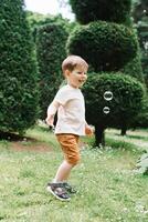 Emotional portrait of a happy and cheerful three-year-old little boy running after soap bubbles on a walk in the park. Happy childhood. photo