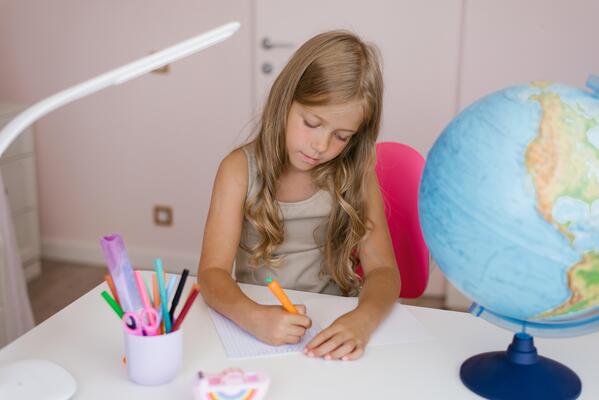 Girl sits at home at a table and write in a notebook, completing a learning task or repeating lessons at home