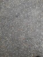 A close-up view of an exposed aggregate concrete surface, consisting of small pebbles and stones embedded in a smooth, gray cement base. The texture is rough and detailed. photo