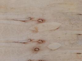 A light colored wooden surface with natural grain patterns and subtle knots. Texture is smooth, with some areas displaying faint lines and color variations, giving it an organic and rustic appearance. photo