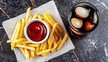 macro shot of french fries on black marble with ketchup and a glass of Coca-Cola with ice photo
