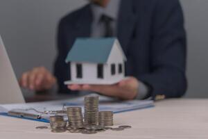 A man in a suit holding a laptop and a house model photo