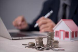 Man in suit sitting at desk with coins and house model photo