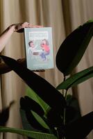 A person holding a book with a plant in the background photo