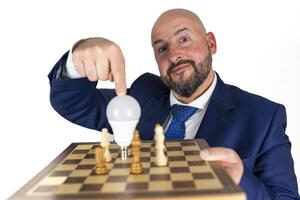 portrait of businessman in blue suit and tie with friendly expression showing light bulb on chessboard as symbol isolated on white background photo