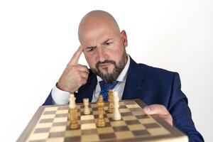 portrait of businessman in blue suit and tie with thoughtful expression looking at chessboard isolated on white background photo