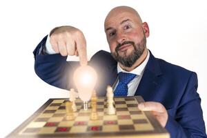 portrait of businessman in blue suit and tie with friendly expression showing light bulb on chessboard as symbol isolated on white background photo