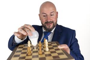 portrait of businessman in blue suit and tie with friendly expression showing light bulb on chessboard as symbol isolated on white background photo
