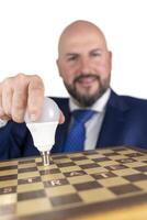portrait of businessman in blue suit and tie with friendly expression showing light bulb on chessboard as symbol isolated on white background photo