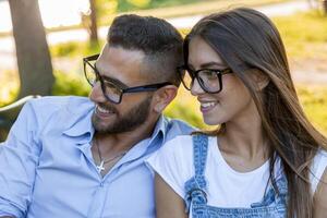 beautiful couple of young adult lovers smiling wearing eyeglasses relaxing sitting on table in park photo