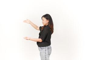 beautiful Asian woman poses with open hands, gesturing toward empty space to showcase a product against a white background photo