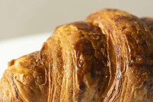 Freshly baked croissant on light background. Single French pastry closeup photo. Buttered bread croissant on white photo