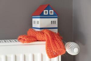 House model wrapped in scarf on radiator indoors. Winter heating efficiency photo