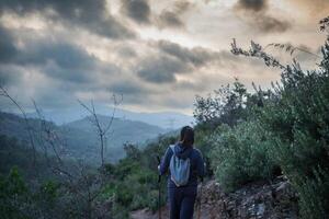 Hiker walks down a mountain path while looking at the sunset sky. photo