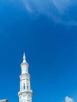 A pristine white minaret, intricately designed, stands tall against a backdrop of a clear, deep blue sky. photo