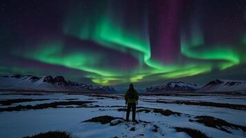 A person standing in the snow looking at the aurora bore photo