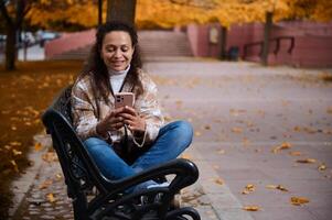 Woman enjoying autumn day on bench while using smartphone photo