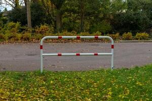 A simple white metal barrier, marked with red reflective strips, is positioned at the edge of a paved road photo