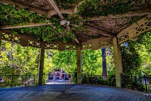 A wooden gazebo with intricate lattice work is adorned with lush green vines, creating a serene and shaded environment in Alcoy photo