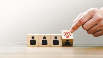 Hand Picking a Block with a Lightbulb Icon Representing Innovation New Ideas, Standing Out Among Wooden Blocks with People Icons, Symbolizing Leadership, Creative Solutions, Individuality in Teamwork photo