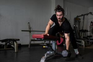 Caucasian man with strong and muscular body is training on bent over row dumbbell with bench to build back and wing muscle inside the gym concept photo