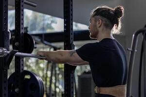 Caucasian muscular body builder sport man is practice weight training on squat barbell for core muscle inside gym with dark background for exercising and workout photo