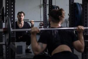 Muscular caucasian body builder sport man is practice weight training on squat barbell for core muscle inside gym with dark background for exercising and workout photo