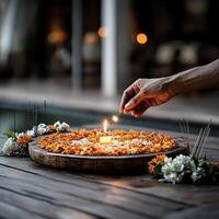 A hand lighting a candle surrounded by vibrant flowers at a serene setting. photo