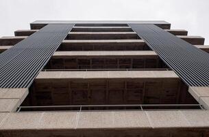 Low angle view of a modern concrete building with vertical elements and textured facade under cloudy sky photo