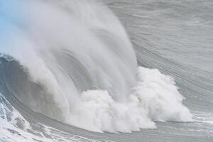 Powerful wave with ocean spray crashing near the coastline at Nazare in Portugal photo