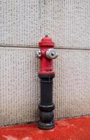 Red fire hydrant with black base mounted on a textured concrete wall with red ground surface photo