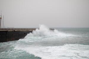 Rough ocean waves crashing powerfully against a concrete pier on a foggy day, with water spraying over the edge and creating a dramatic scene photo